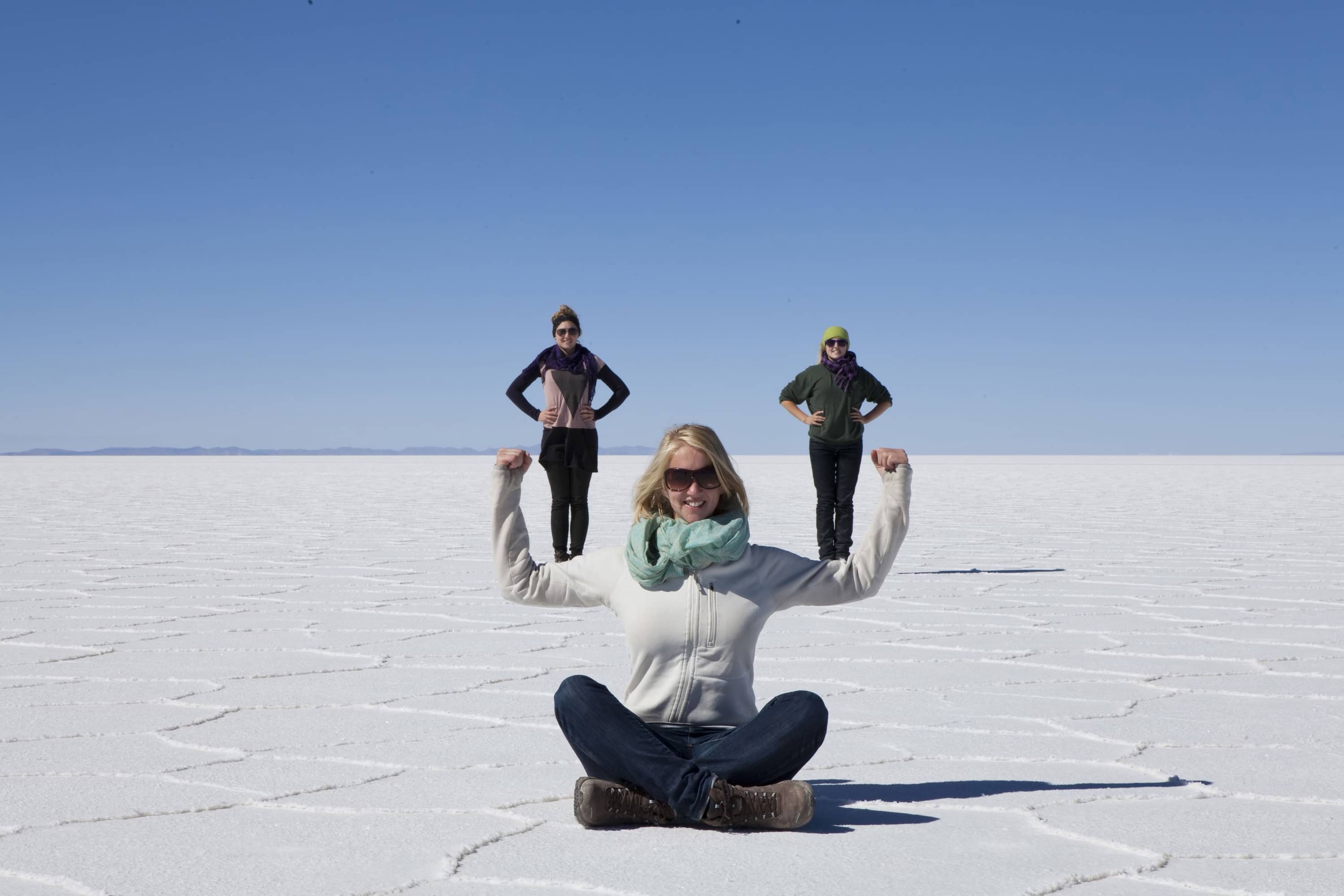 A photo of a woman balancing two friends on her biceps taken using forced perspective in the Uyuni Salt Flats in Bolivia