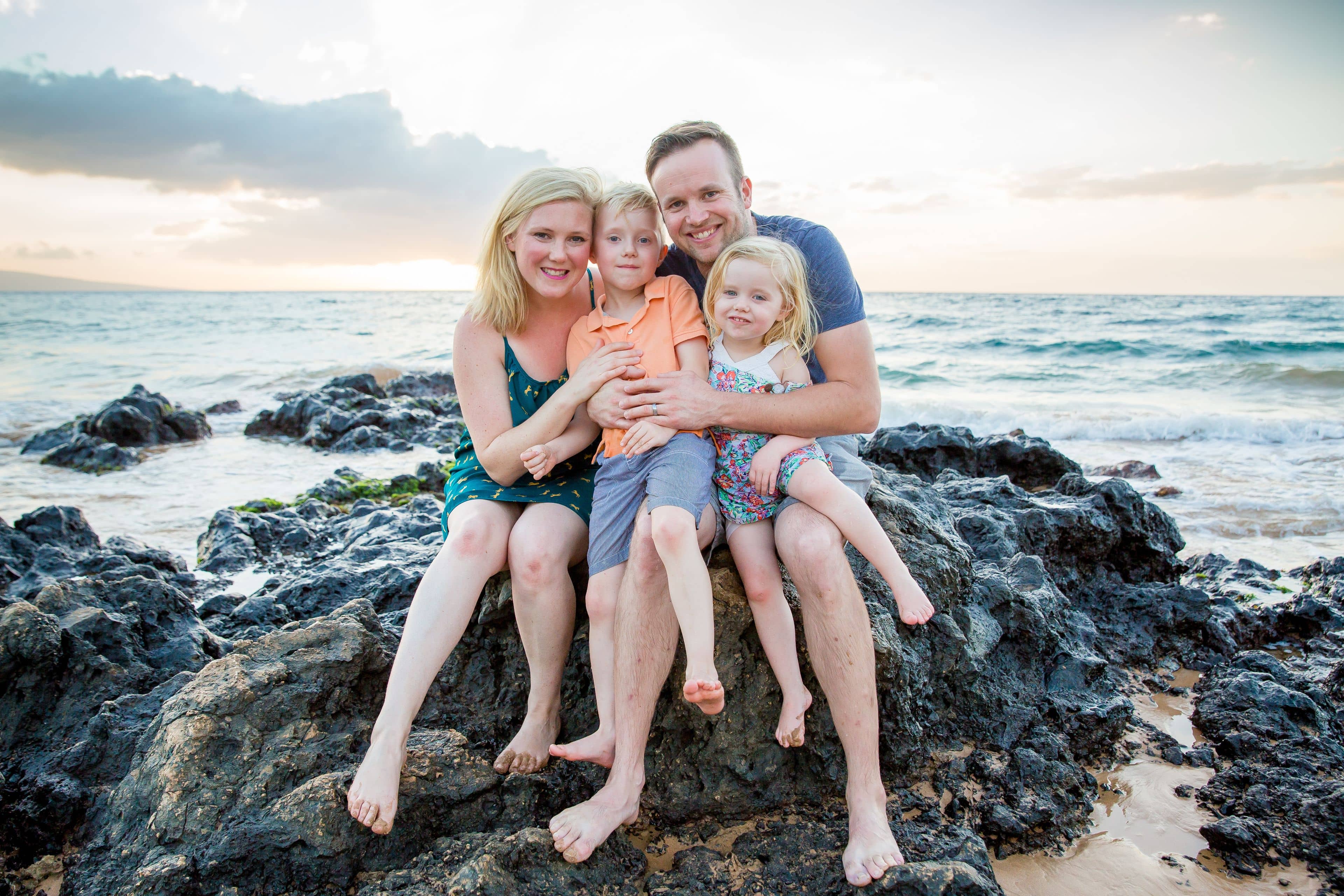 Family portrait of a family of four sitting on a rock on the beach in Maui