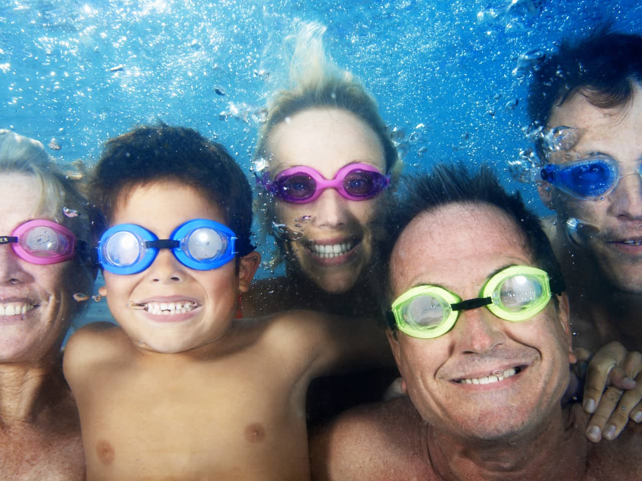 Family wearing colofrul goggles and smiling under water in a pool