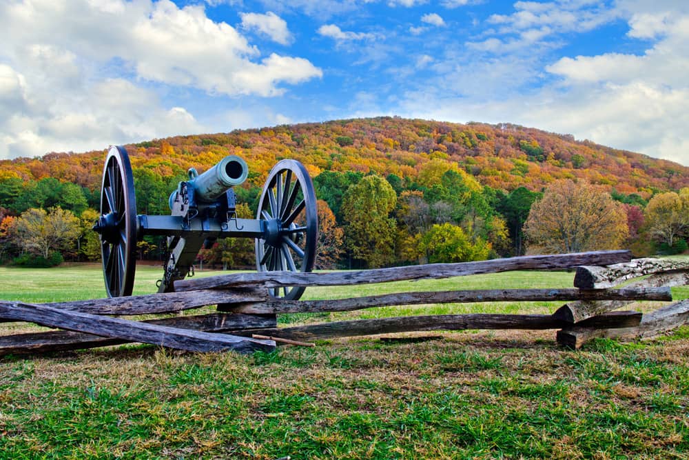 A historical cannon near a wooden fence with a backdrop of changing autumn leaves and a blue sky at Kennesaw Mountain National Battlefield Park—a great free thing to do with kids in Atlanta.